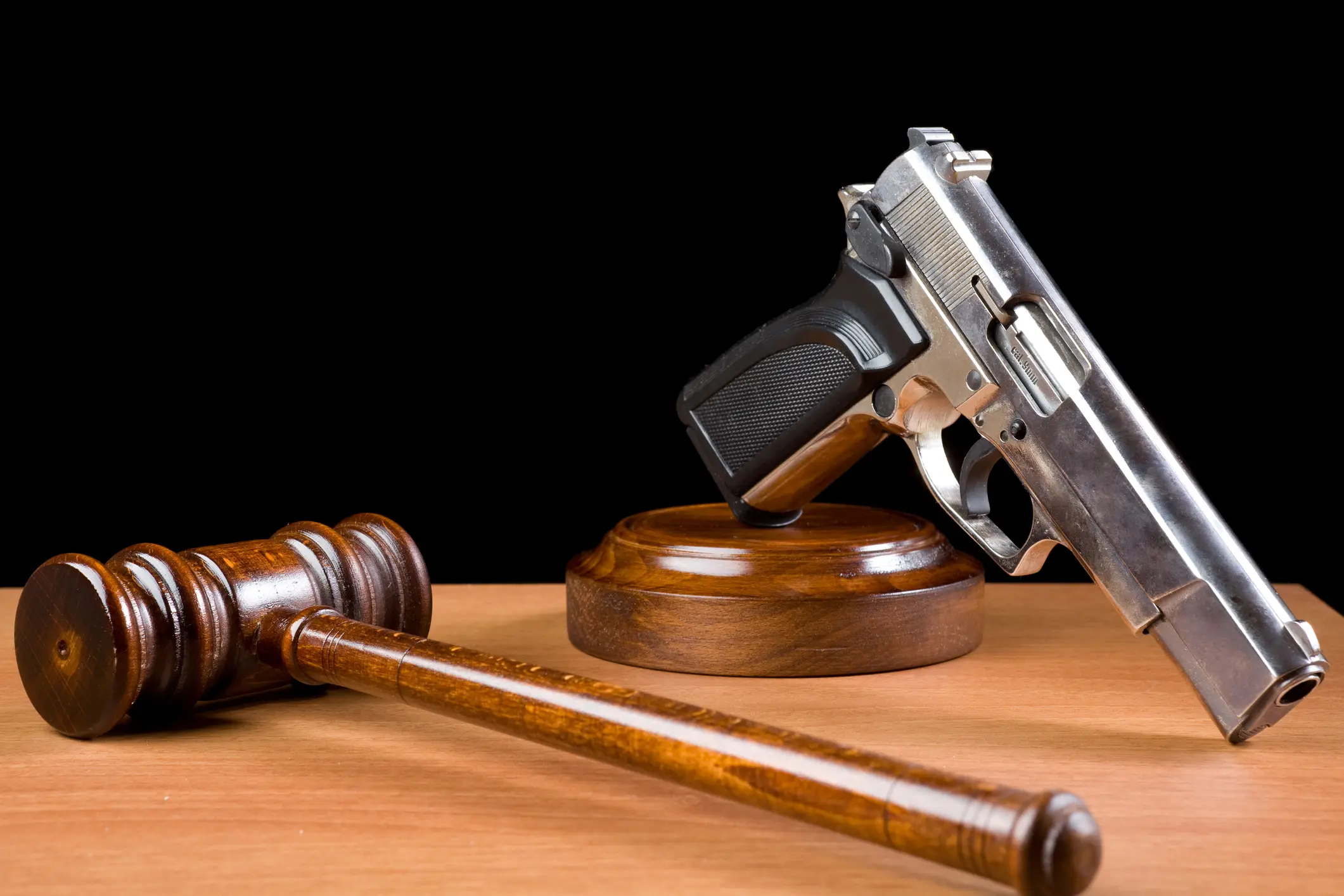 Wooden Gavel And Handgun On Table For Crime Punishment Concept Wooden Gavel And Handgun On Table For Crime Punishment Concept.The background is black.The gun is placed on the right of frame while gavel is seen on the right side.The desk is brown wood.The photo was shot with a full frame DSLR camera in horizontal composition and in studio.Nobody is seen in photo.